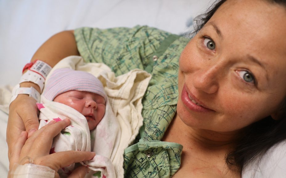 A mother, still wearing her hospital ID bracelet, holding her newborn baby in the birth center